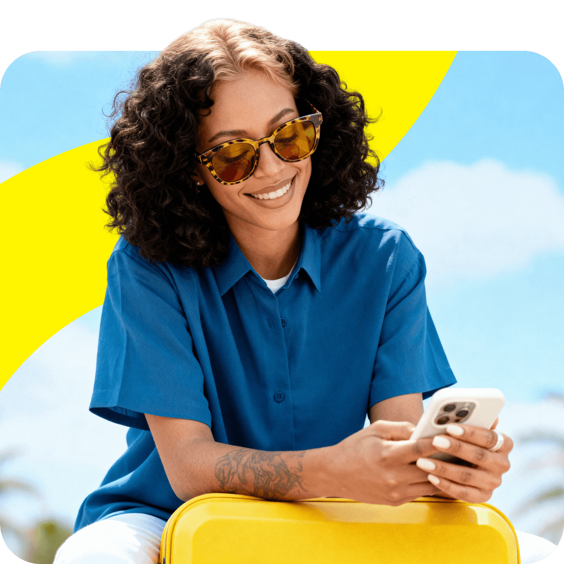 Uma mulher sorridente utiliza o telemóvel enquanto está sentada com a sua bagagem.