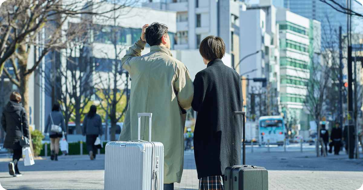 Two people standing in front of a building with two suitcases