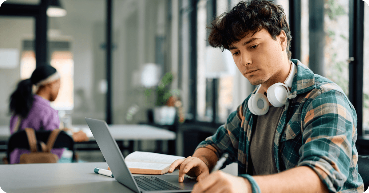 A man wearing headphones, working on a laptop to research an international travel checklist.