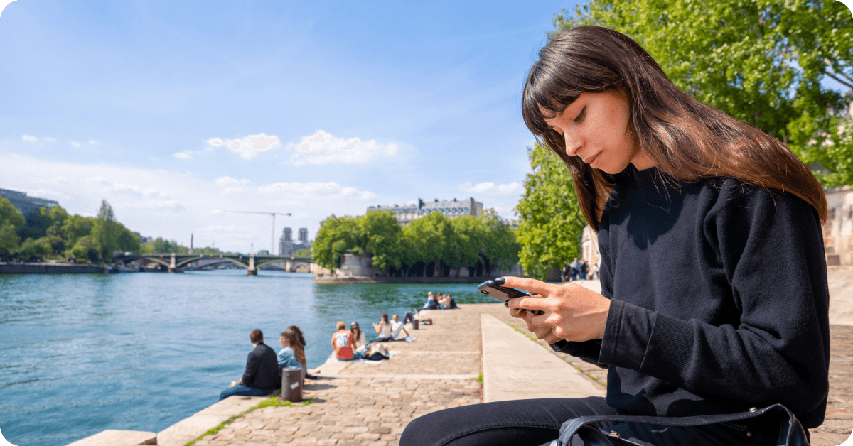 A person with a phone in their hands walking by then Seine