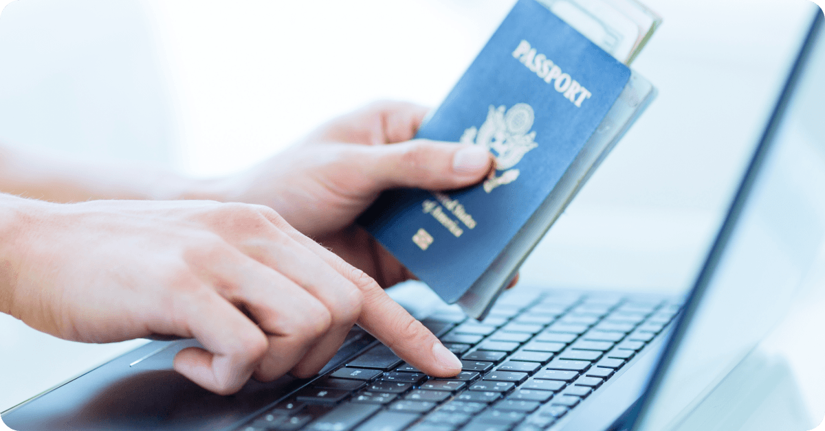 A person holding a passport while checking something on a laptop.
