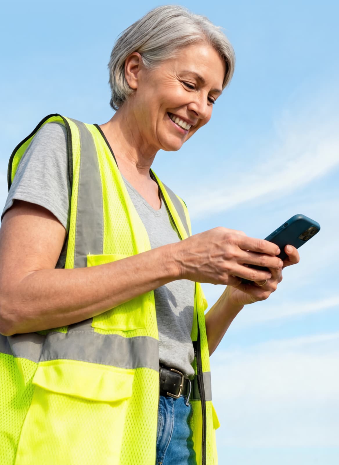 A smiling nonprofit field worker in a safety vest using a smartphone to stay connected.