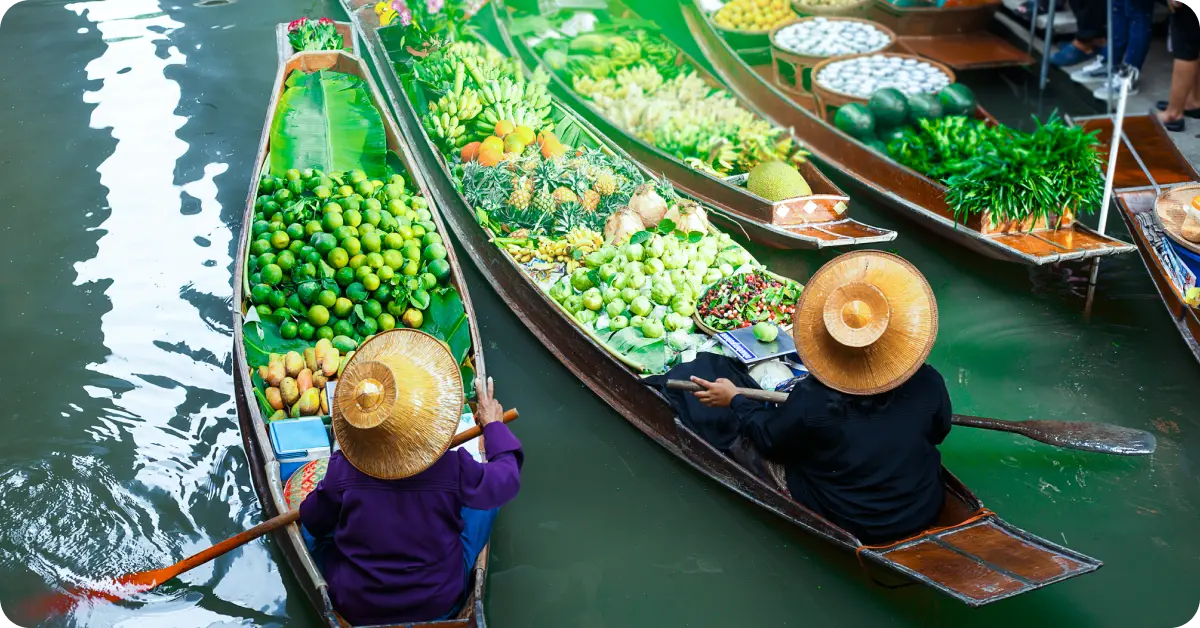 Two vendors in boats selling fruit at a floating market in Thailand.