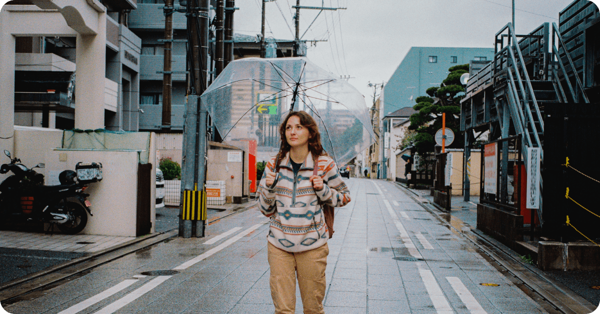 A tourist walking through a rain-soaked alley with a clear umbrella.