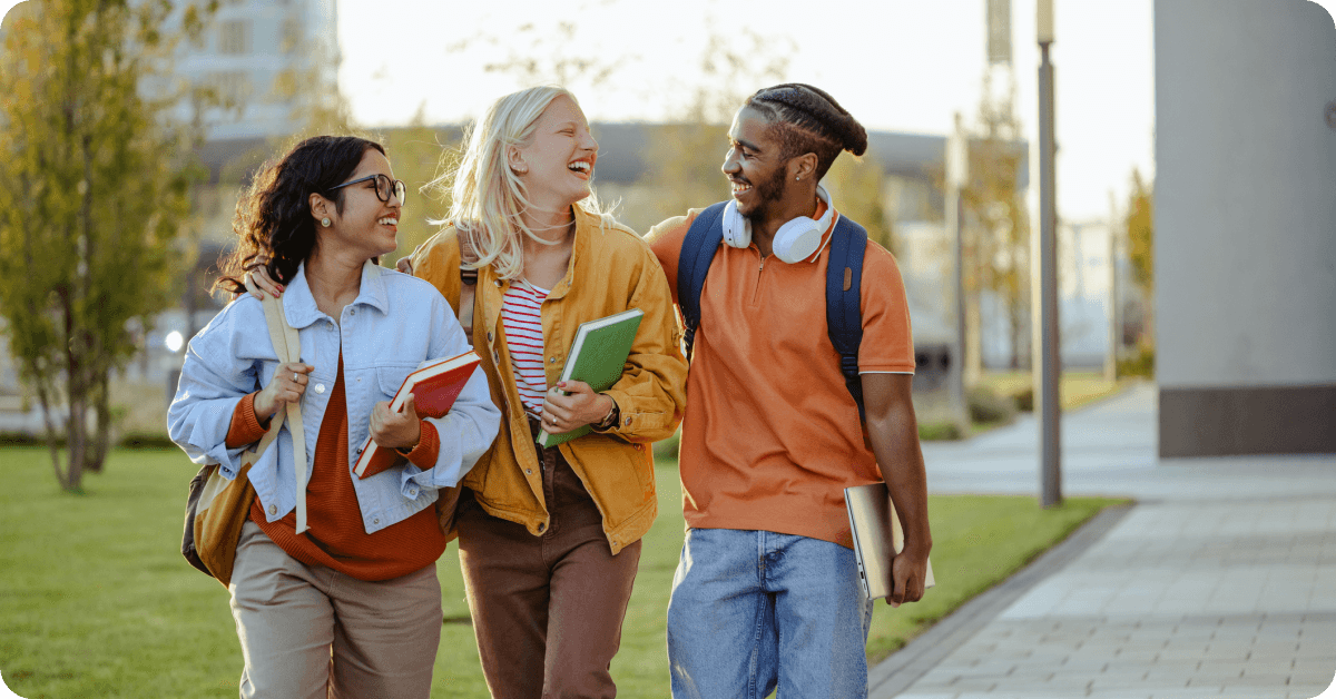 Three students are walking on a university campus and laughing.